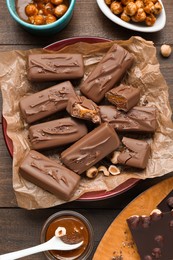 Photo of Delicious chocolate candy bars and nuts on wooden table, flat lay