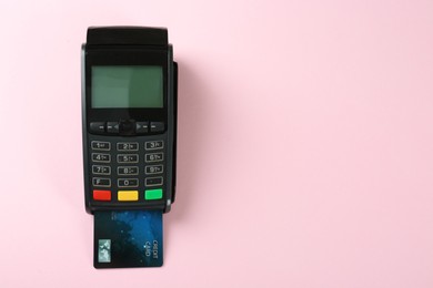 Photo of New modern payment terminal with credit card on pink background, top view. Space for text