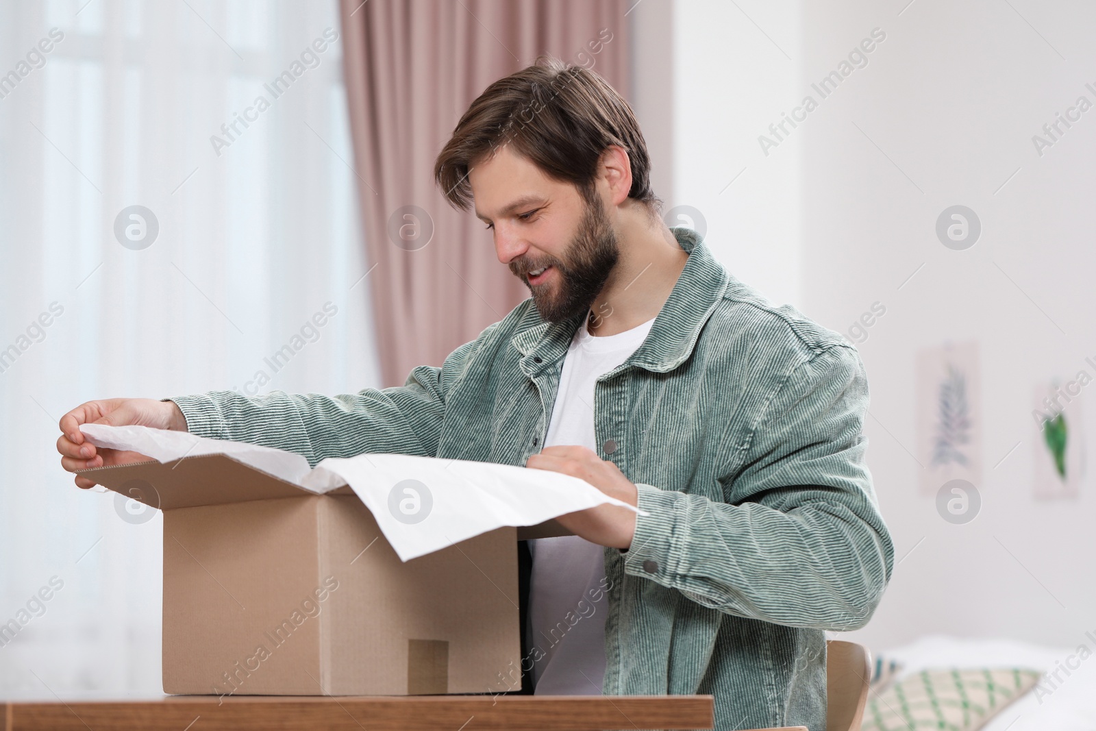 Photo of Happy man opening parcel at home. Internet shopping