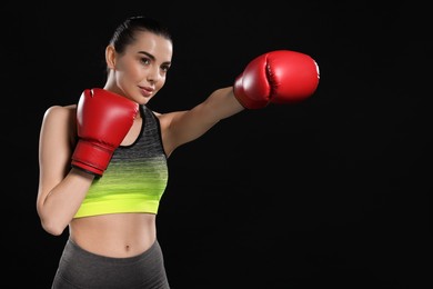 Photo of Beautiful woman in boxing gloves training on black background. Space for text