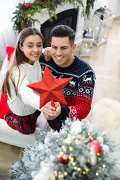 Photo of Couple decorating Christmas tree with star topper indoors, above view