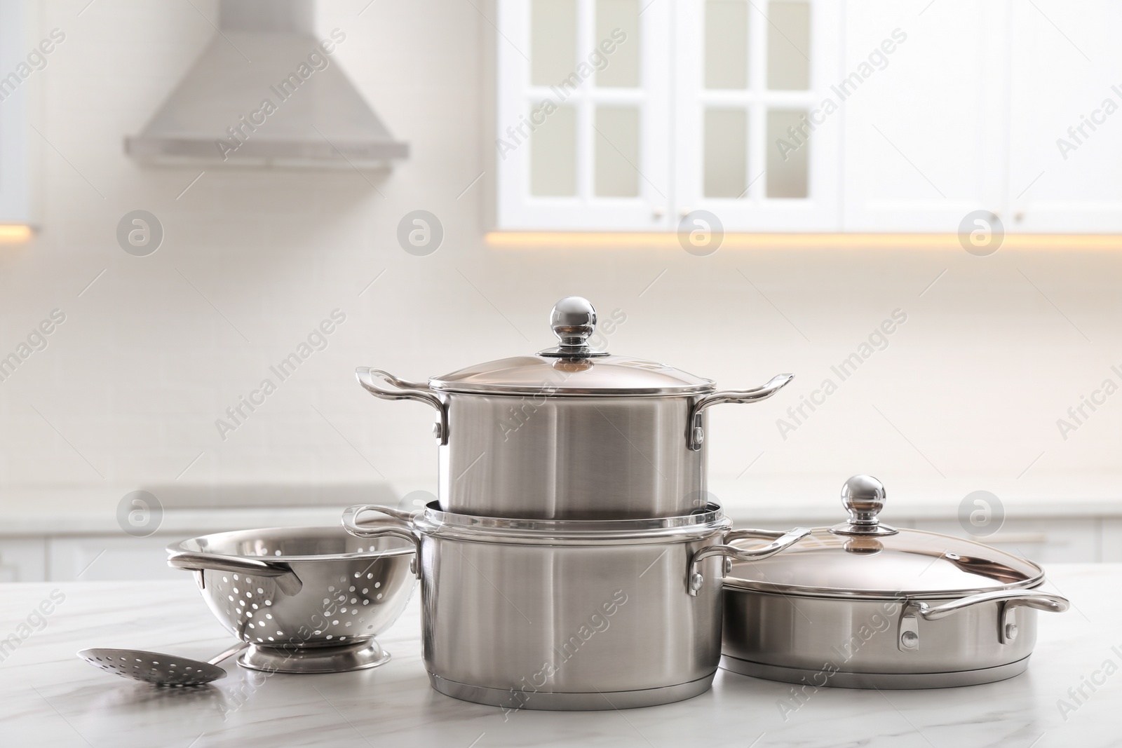 Photo of Set of stainless steel cookware and kitchen utensils on white table indoors