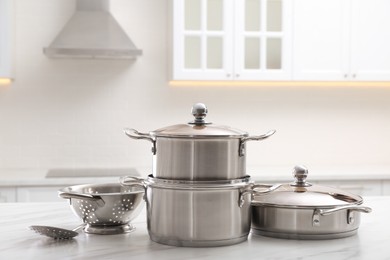 Set of stainless steel cookware and kitchen utensils on white table indoors