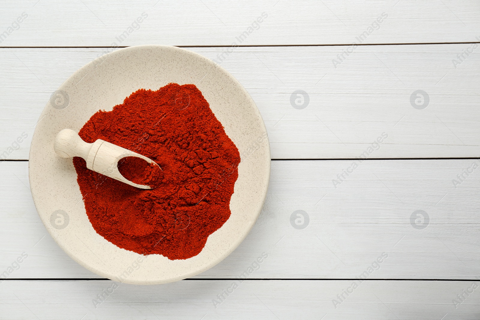 Photo of Plate of aromatic paprika on white wooden table, top view. Space for text