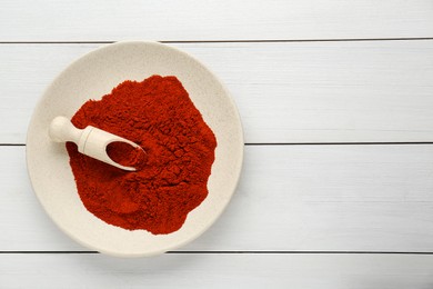 Plate of aromatic paprika on white wooden table, top view. Space for text