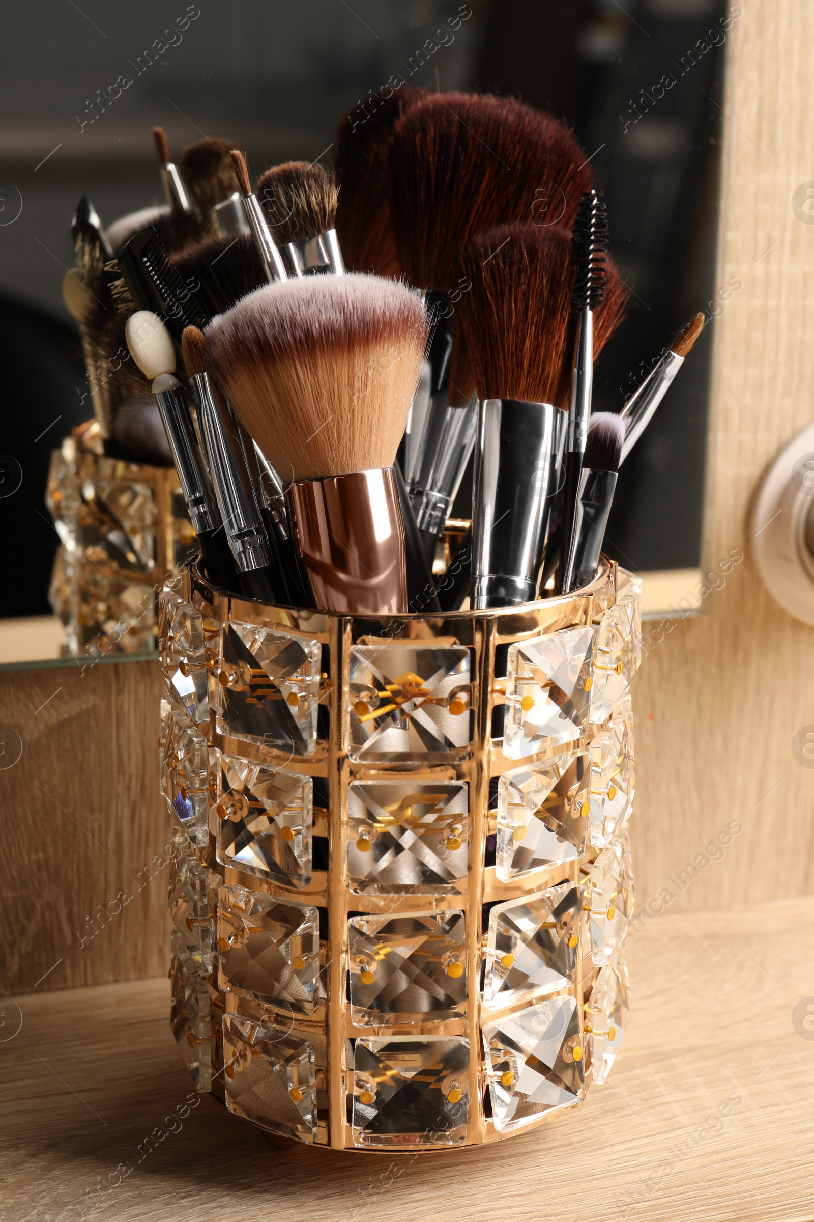 Photo of Set of professional makeup brushes near mirror on wooden table