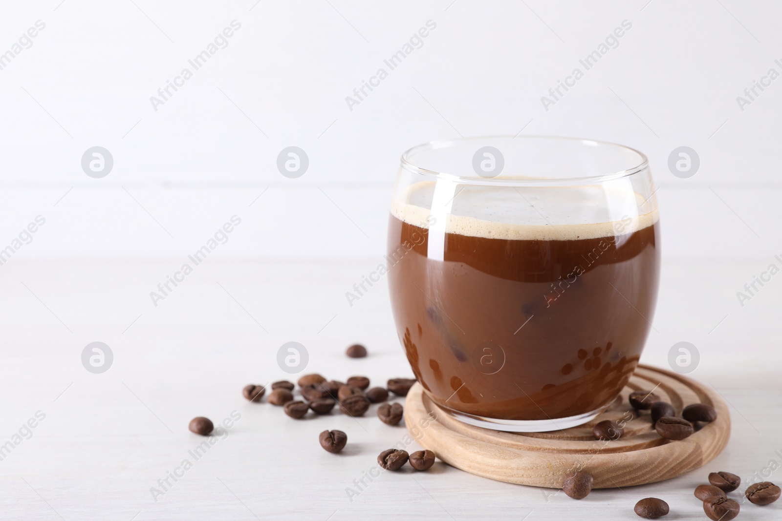 Photo of Refreshing iced coffee with milk in glass and beans on white wooden table, space for text