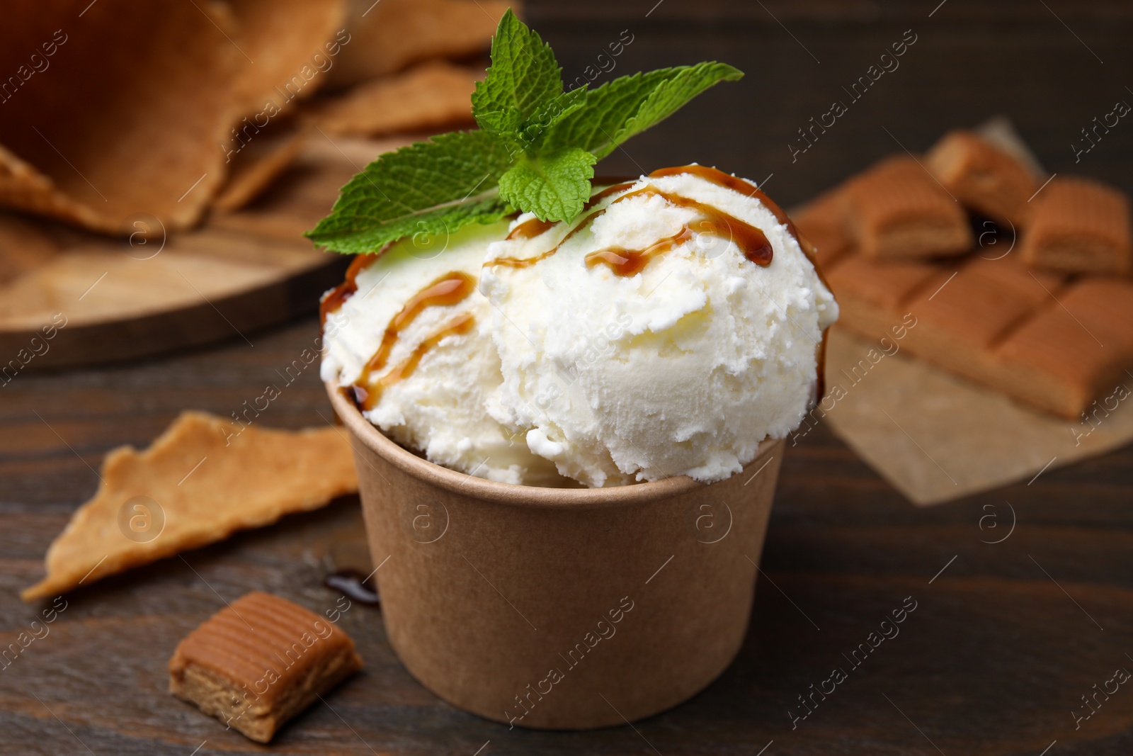Photo of Scoops of tasty ice cream with caramel sauce, mint leaves and candies on wooden table, closeup