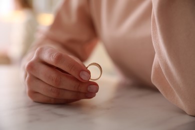Photo of Woman holding wedding ring at table indoors, closeup. Divorce concept