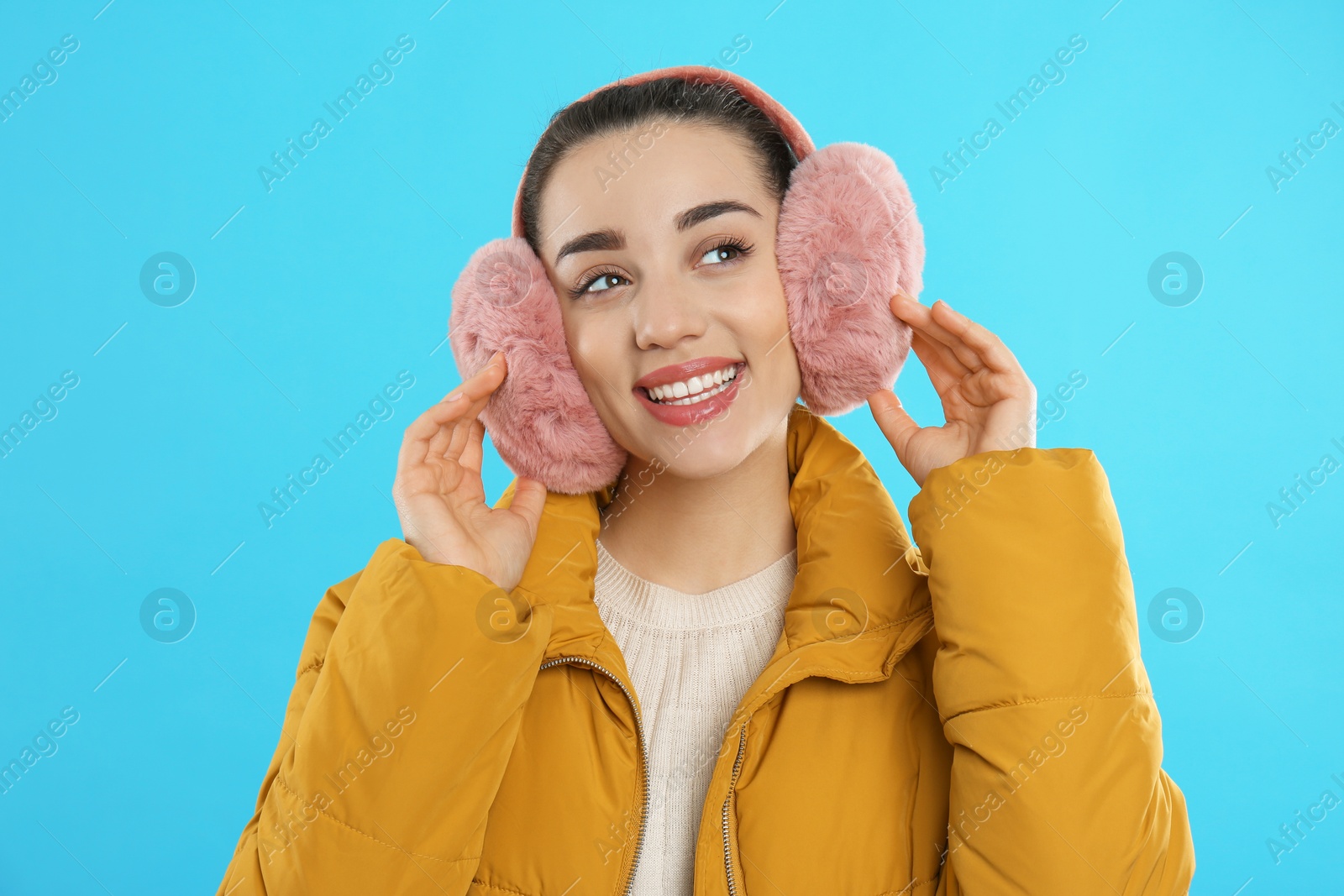 Photo of Beautiful young woman wearing earmuffs on light blue background