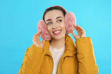 Photo of Beautiful young woman wearing earmuffs on light blue background