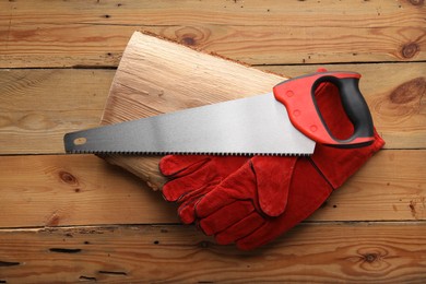 Saw with colorful handle and gloves on wooden background, top view