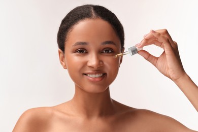 Smiling woman applying serum onto her face on white background