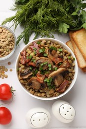 Photo of Delicious lentils with mushrooms, bacon and green onion in bowl served on white table, flat lay