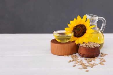 Photo of Sunflower, oil and seeds on white wooden table, space for text