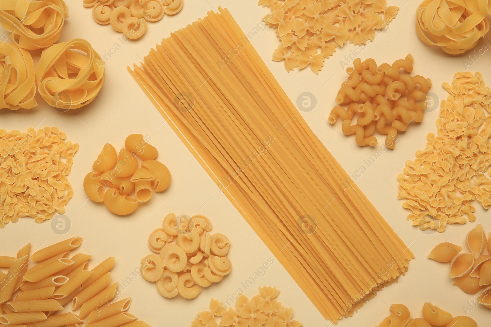 Photo of Different types of pasta on beige background, flat lay