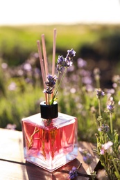 Photo of Reed air freshener on wooden table in blooming lavender field