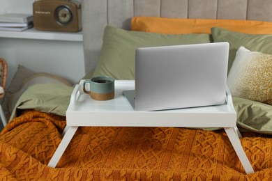Photo of White tray with modern laptop and cup of aromatic tea on bed indoors