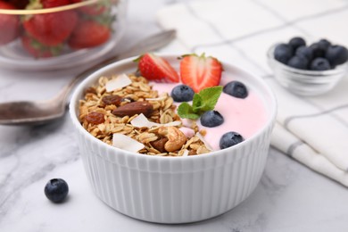 Photo of Tasty granola, yogurt and fresh berries in bowl on white marble table, closeup. Healthy breakfast
