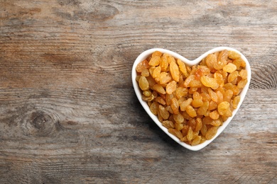 Heart shaped plate with raisins and space for text on wooden background, top view. Dried fruit as healthy snack