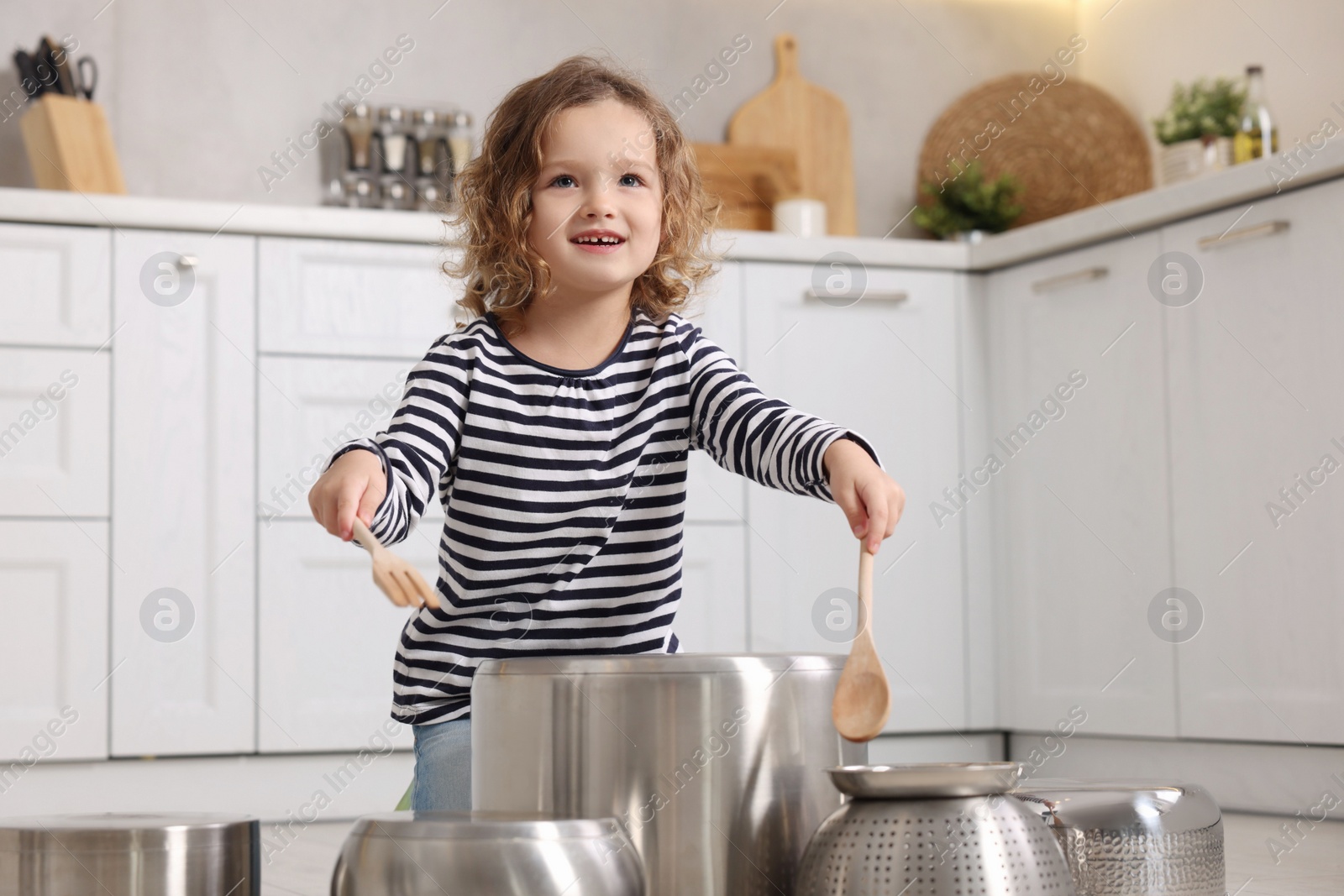 Photo of Little girl pretending to play drums on pots in kitchen