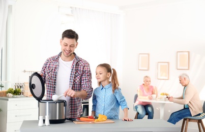 Father and daughter preparing food with modern multi cooker in kitchen