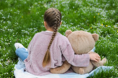 Little girl with teddy bear on plaid outdoors, back view