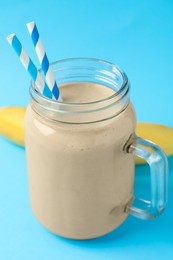 Mason jar of tasty banana smoothie with straws and fresh fruit on light blue background
