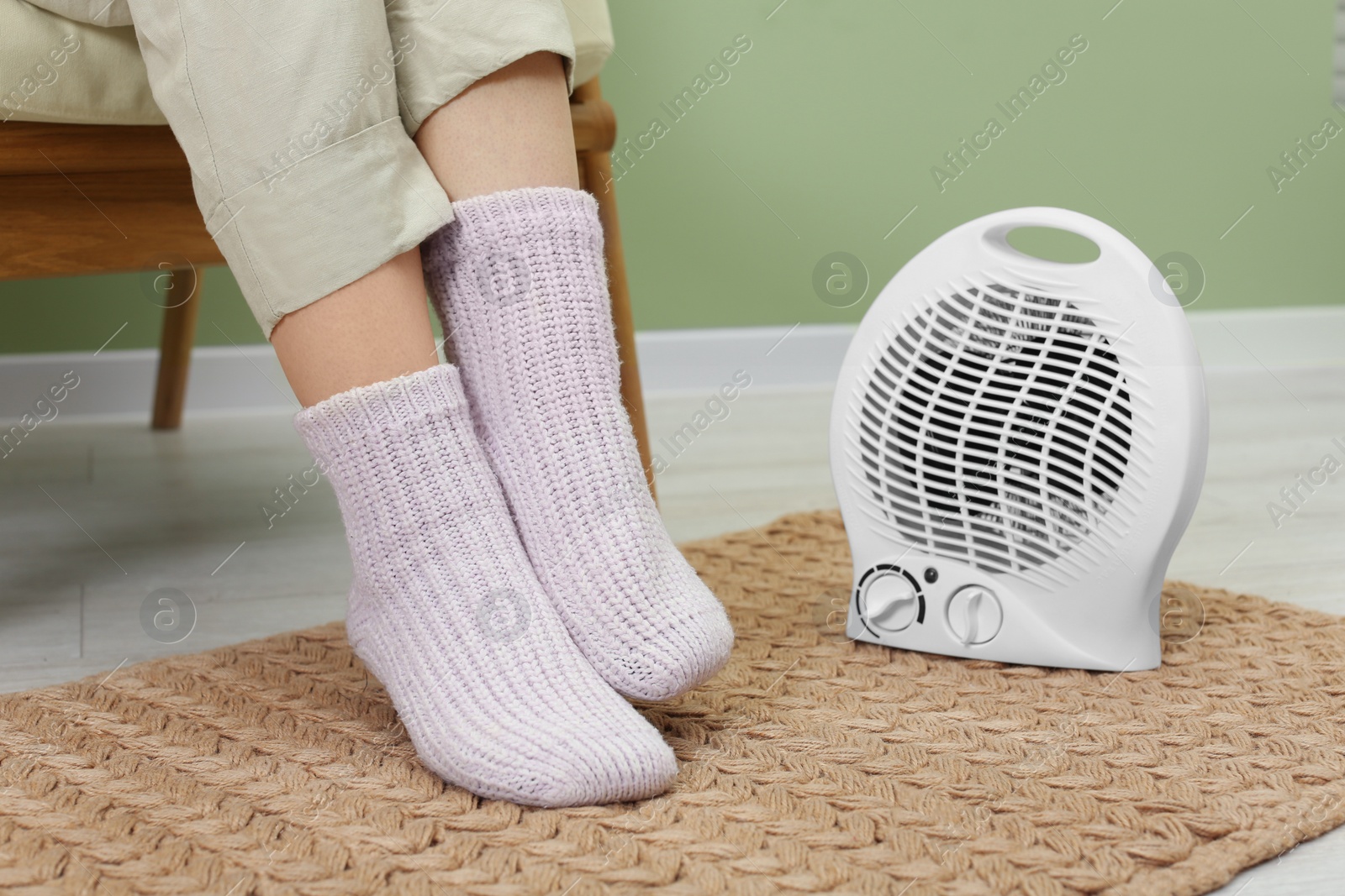 Photo of Woman warming feet near electric fan heater at home, closeup