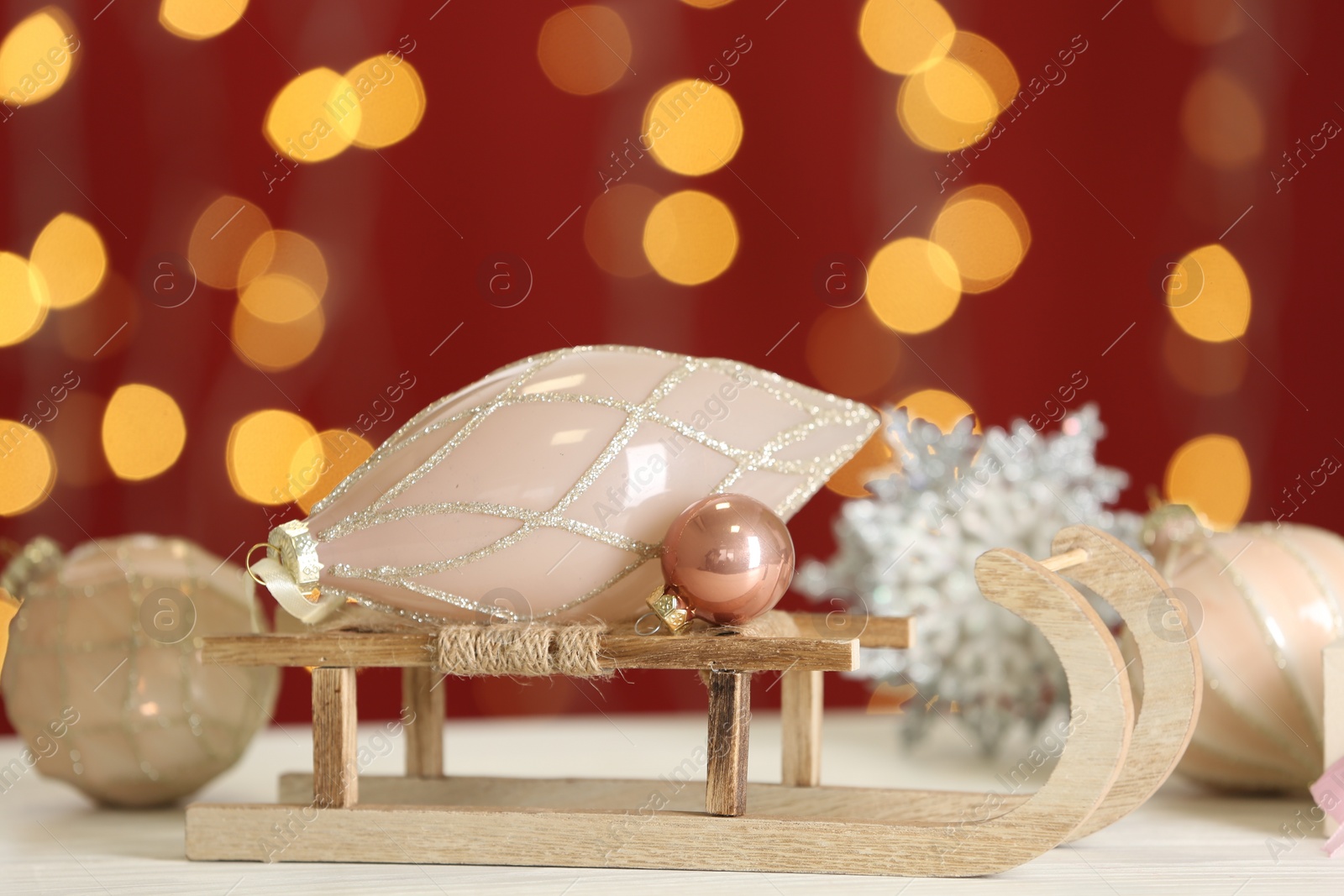 Photo of Decorative sleigh with Christmas ornaments on white table against blurred lights