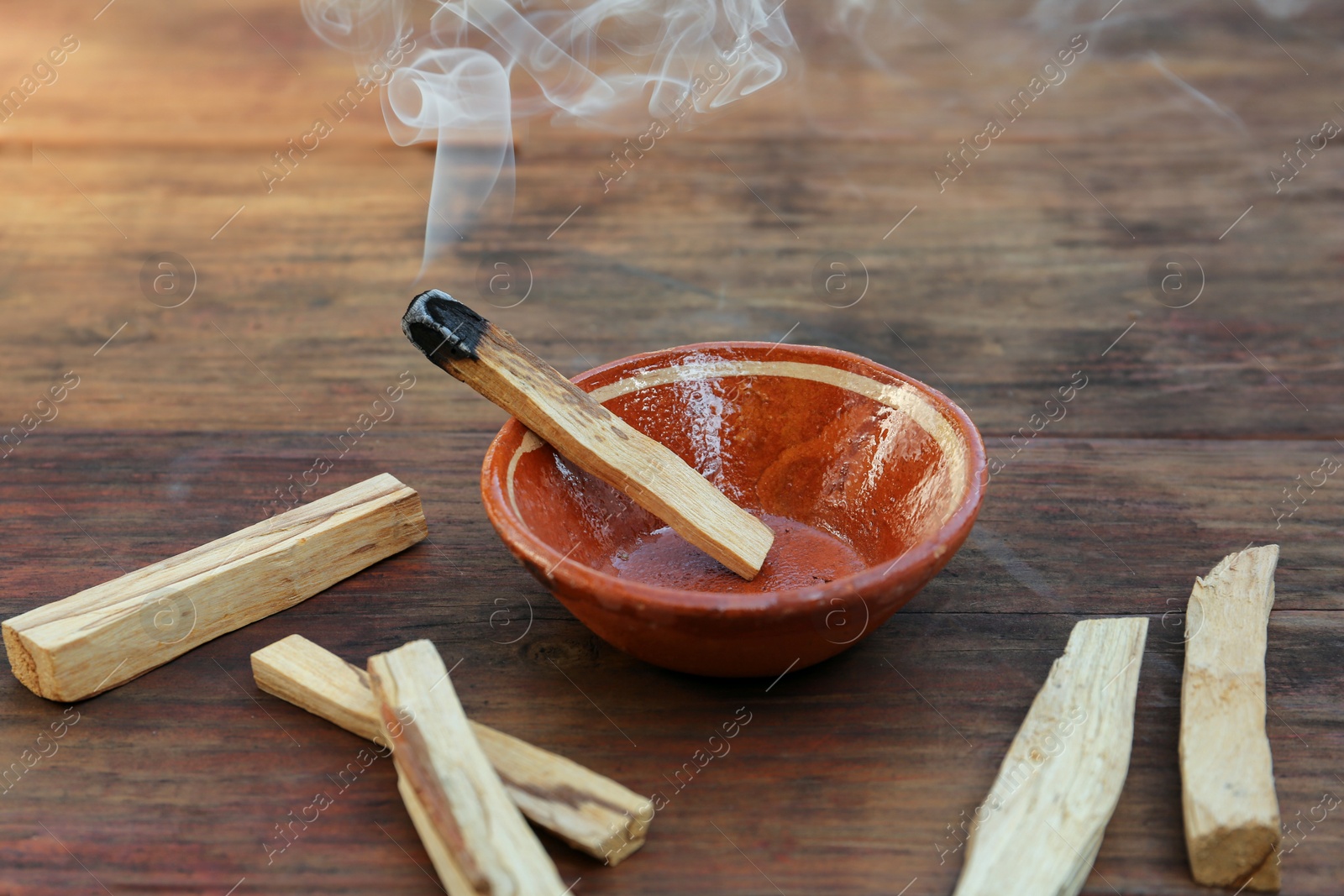 Photo of Palo santo stick smoldering in bowl on wooden table