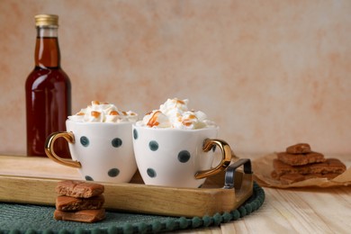 Delicious coffee with whipped cream and caramel syrup on wooden table, space for text