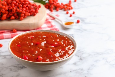 Photo of Delicious rowan jam in bowl and berries on white marble table. Space for text