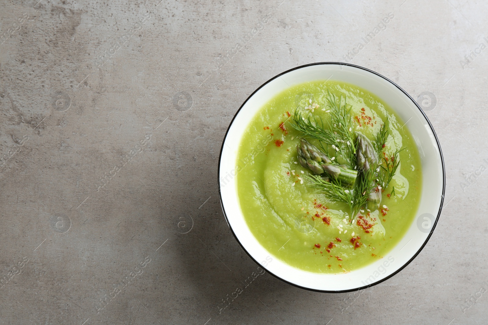 Photo of Delicious asparagus soup in bowl on grey table, top view. Space for text