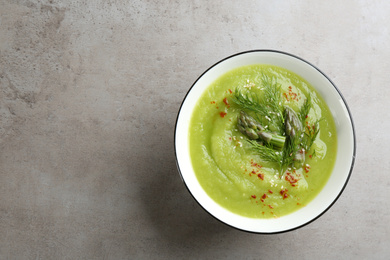Photo of Delicious asparagus soup in bowl on grey table, top view. Space for text