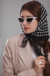 Young woman with sunglasses and stylish bandana on grey background