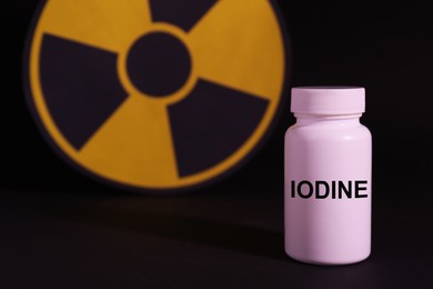 Photo of Plastic container of medical iodine and radiation sign on black background, space for text
