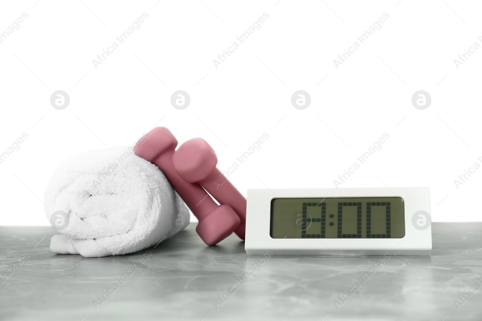 Photo of Digital clock, towel and dumbbells on marble table against grey background. Morning exercise