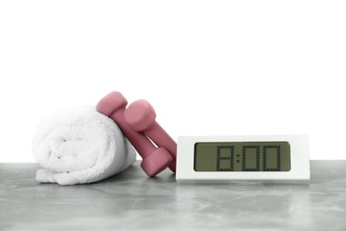 Photo of Digital clock, towel and dumbbells on marble table against grey background. Morning exercise