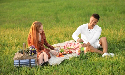 Happy young couple with wine and glasses having picnic in green park