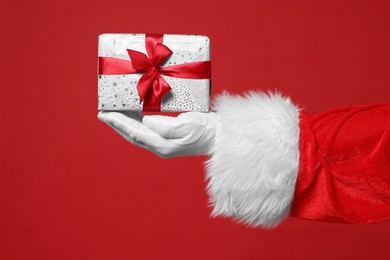 Photo of Santa Claus holding Christmas gift on red background, closeup