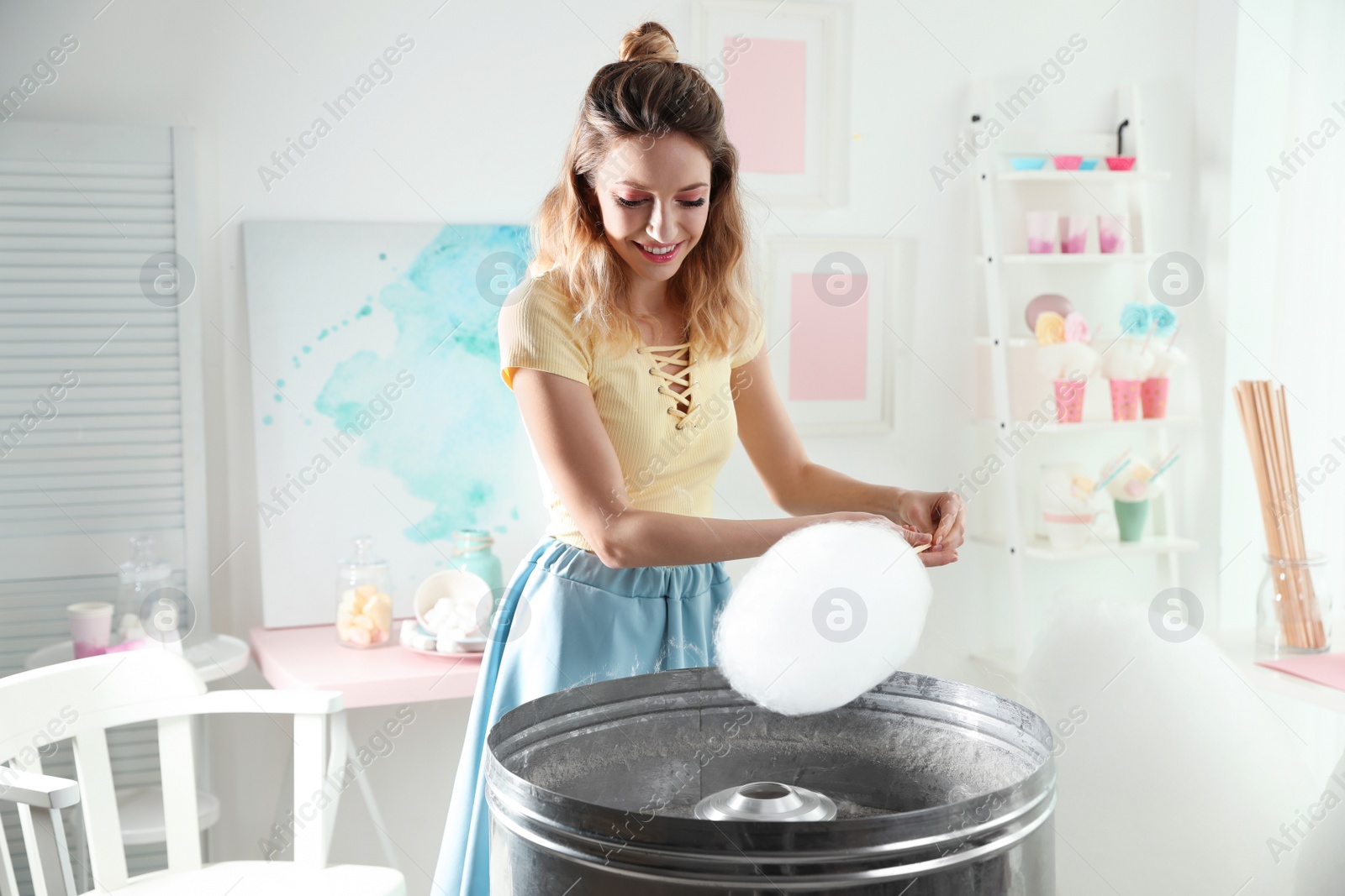 Photo of Young woman making cotton candy using modern machine in room