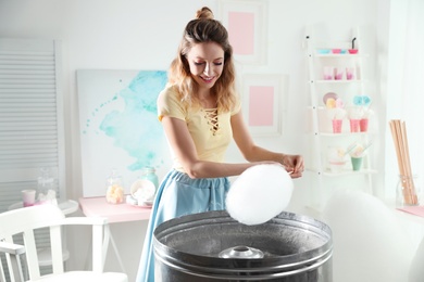 Photo of Young woman making cotton candy using modern machine in room