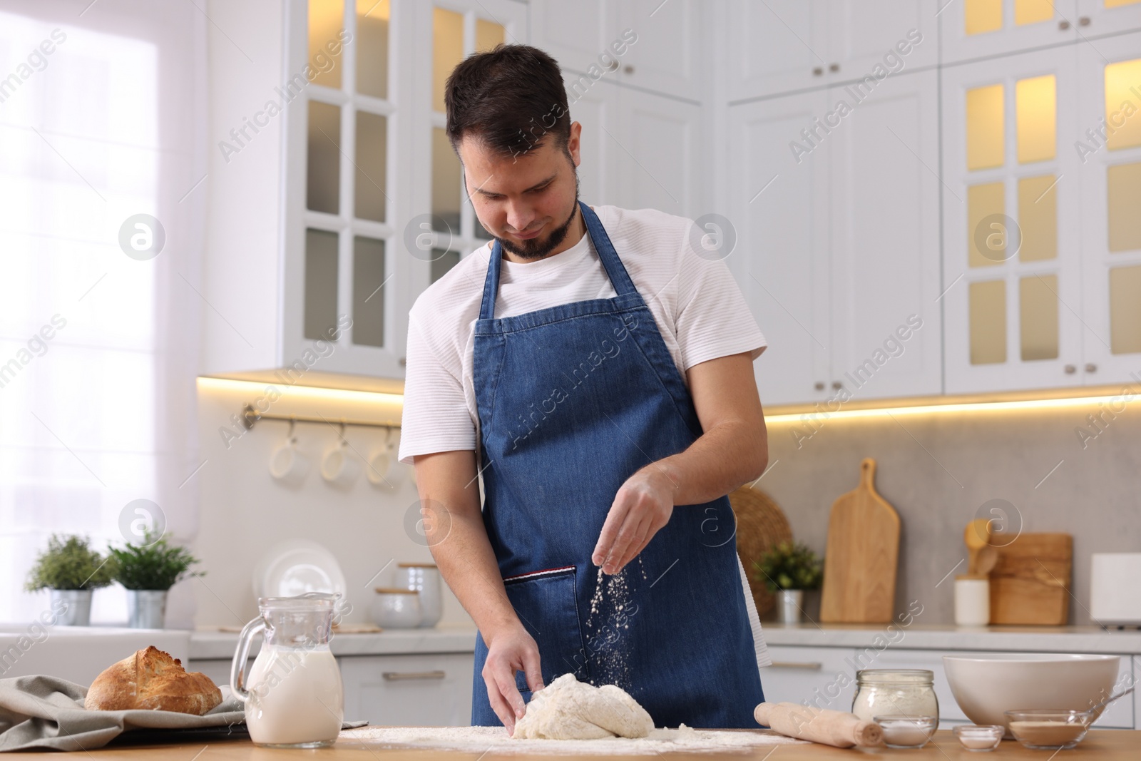 Photo of Making bread. Man sprinkling flour onto dough at wooden table in kitchen