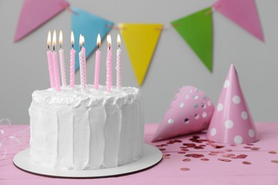 Photo of Delicious cake with burning candles and party hats on pink wooden table. Space for text