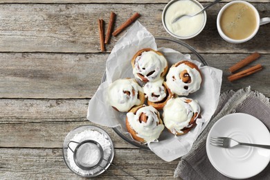 Photo of Tasty cinnamon rolls with cream on wooden table, flat lay. Space for text