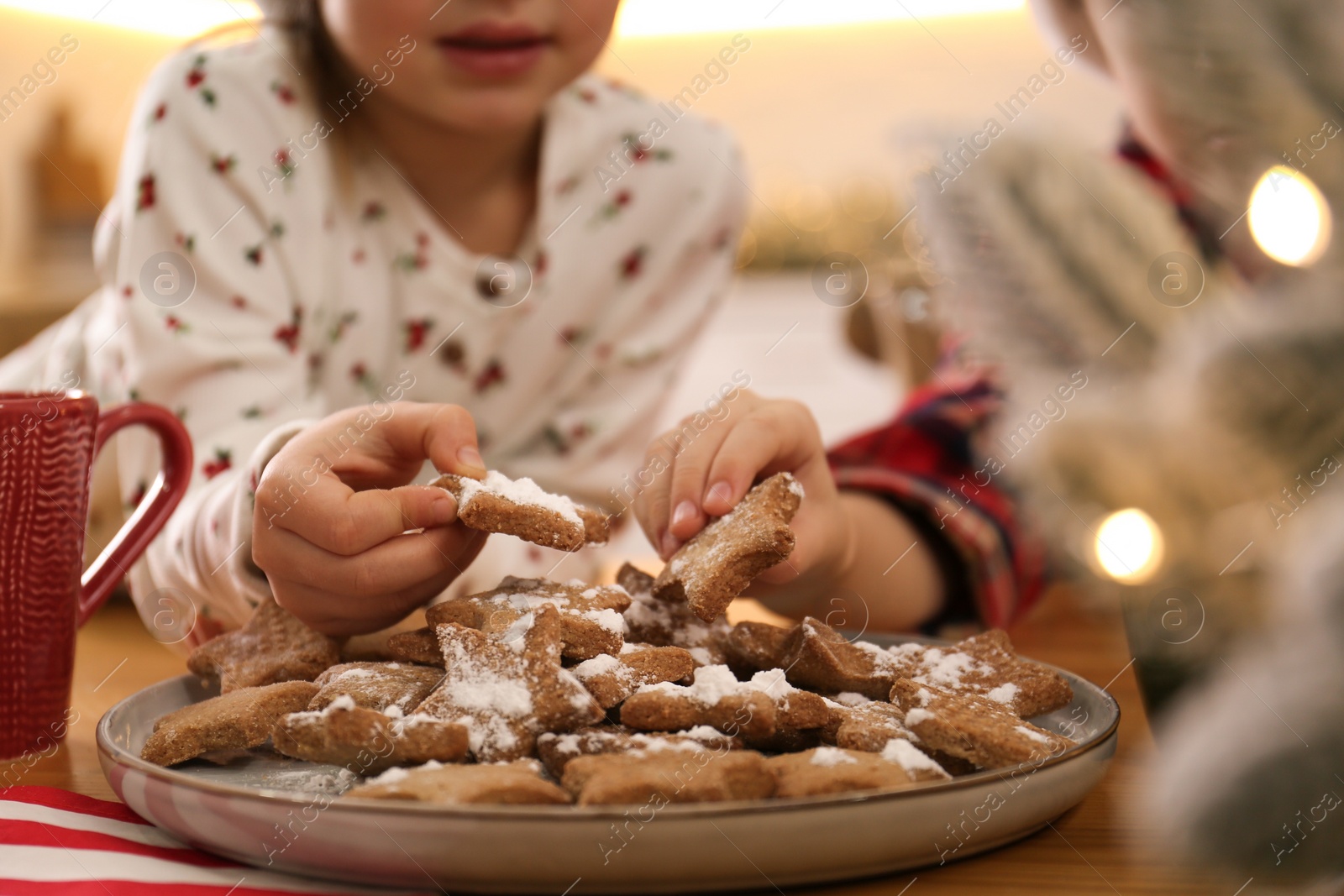 Photo of Little children taking tasty Christmas cookies from plate at table, closeup