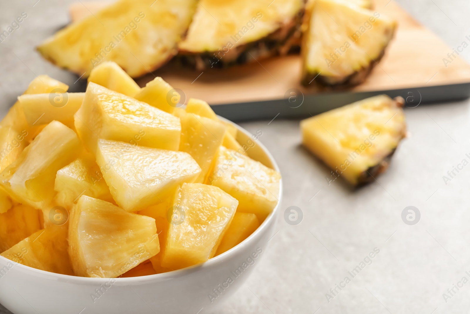 Photo of Bowl with fresh pineapple slices on grey background, closeup