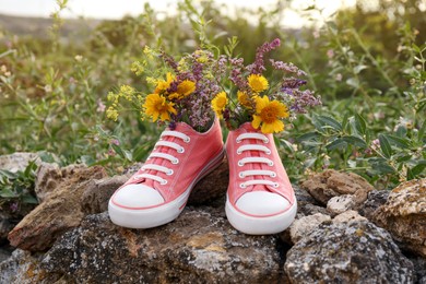 Shoes with beautiful flowers on stones outdoors