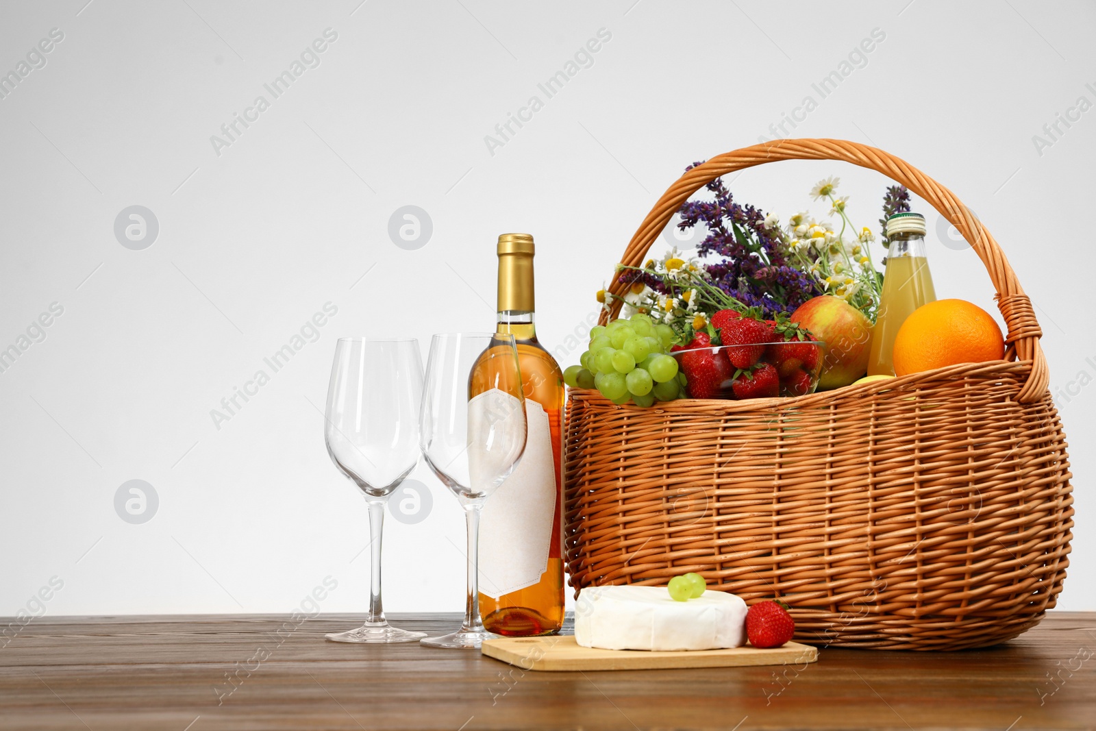 Photo of Picnic basket with wine and products on wooden table against white background. Space for text